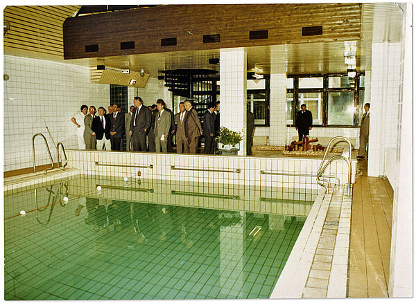Rundgang hochrangiger Stasi-Offiziere durch das Stasi-Ferienheim "Am Rennsteig" im thüringischen Masserberg anlässlich seiner Eröffnung im September 1986; Quelle: BArch, MfS, SdM, Fo, Nr. 28, Bild 7 Blick in eine kleine Schwimmhalle in einem neuen Stasi-Hotel über den Pool hinweg auf eine Gruppe von Herren, die sich die Anlage anlässlich der Einweihung des Hotelgebäudes ansehen.