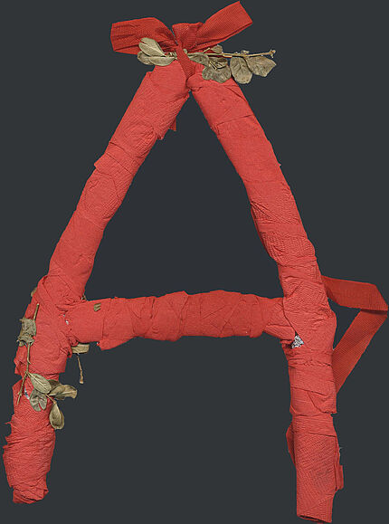Ein aus rotem Krepppapier gebasteltes "A", verziert mit getrockneten Blättern.